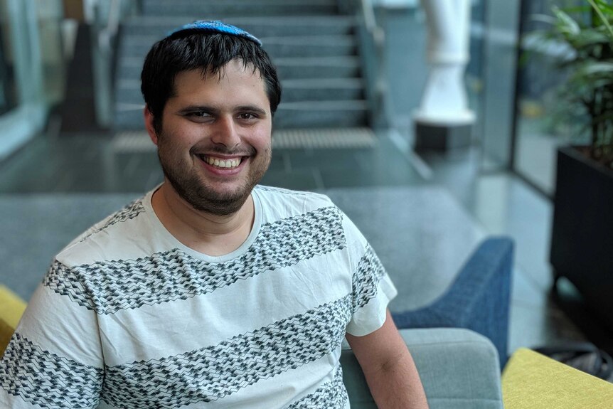 A young man wearing a Jewish head covering smiling and sitting