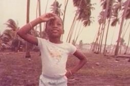 Young Melanie McCollin-Walker stands in front of palm trees in Barbados.
