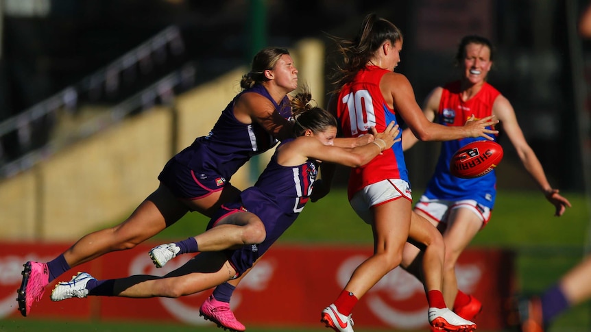 Two players from the Freemantle Dockers tackle a Demons' player in a AFLW match in Perth