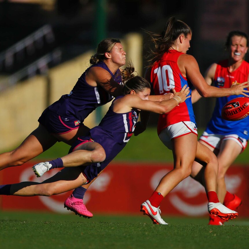 Two players from the Freemantle Dockers tackle a Demons' player in a AFLW match in Perth