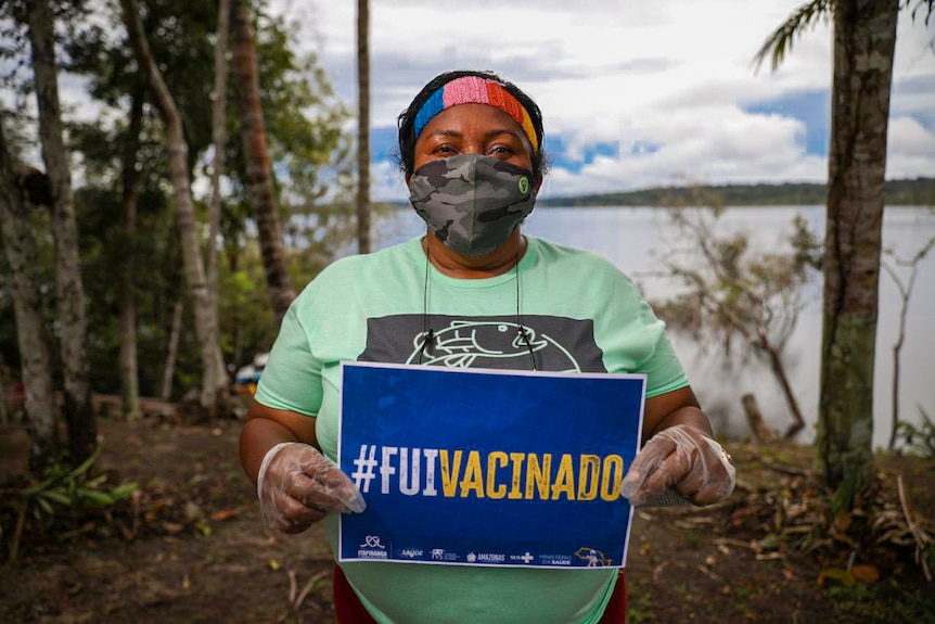 Mulher brasileira segura uma placa na margem de um rio dizendo 'Fui vacinada'