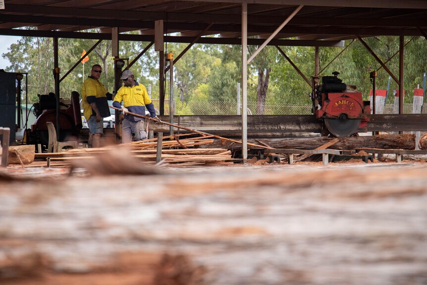 Two men wear high vis shirts while working in a sawmill