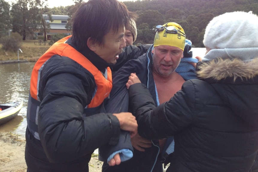 Man emerges from water after swimming as people hurry to warm him up
