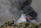 A helicopter waterbombing in front of a dark plume of smoke