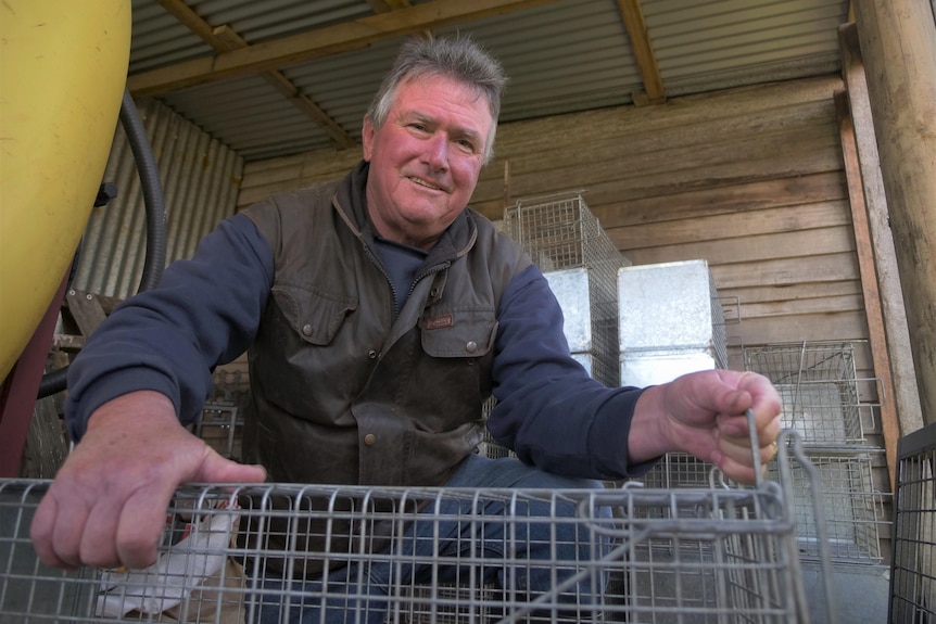 A man in an oilskin vest holding onto a metal cage, smiling to camera.