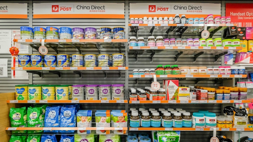 Shelves stacked with baby formula and vitamins. Signs above the shelves read Australia Post and China Direct.