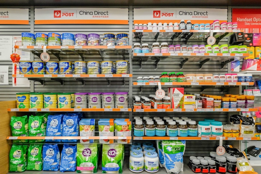 Shelves stacked with baby formula and vitamins. Signs above the shelves read Australia Post and China Direct.