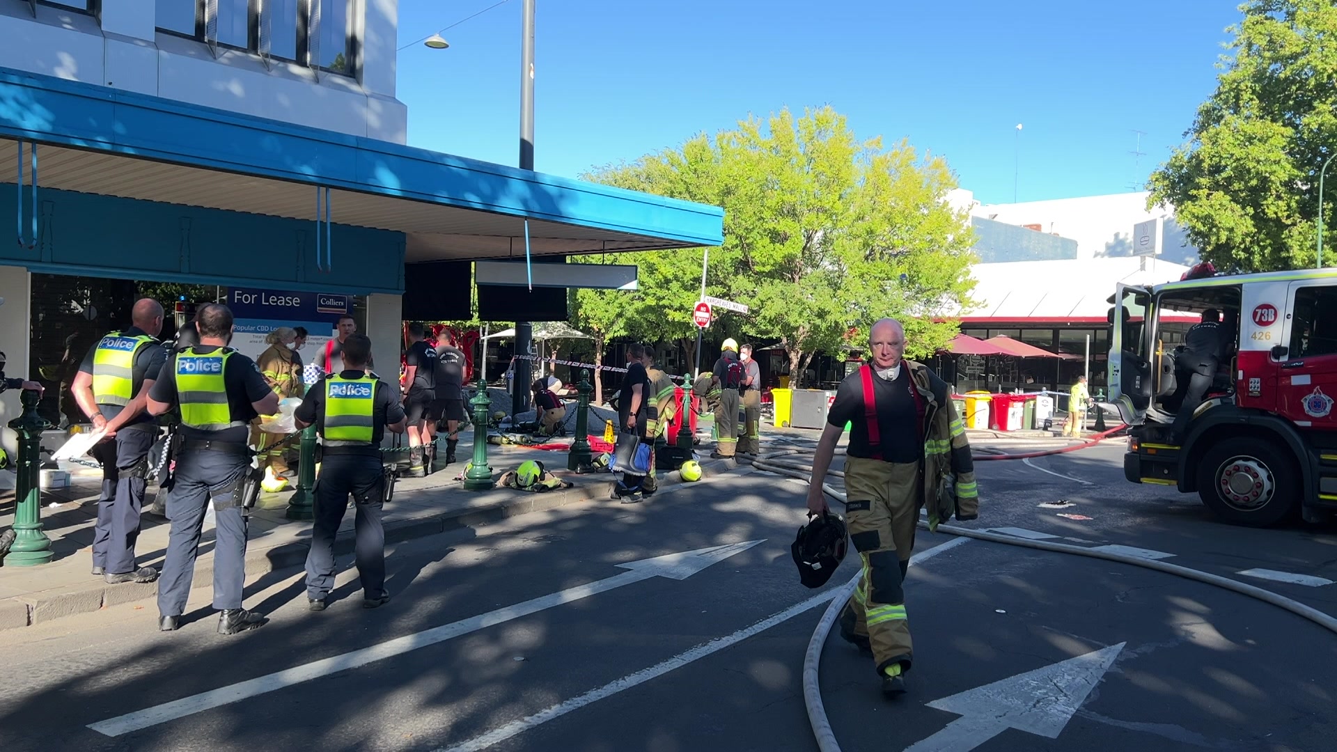 Police wearing yellow high-vis vests gather on the street around a storefront.