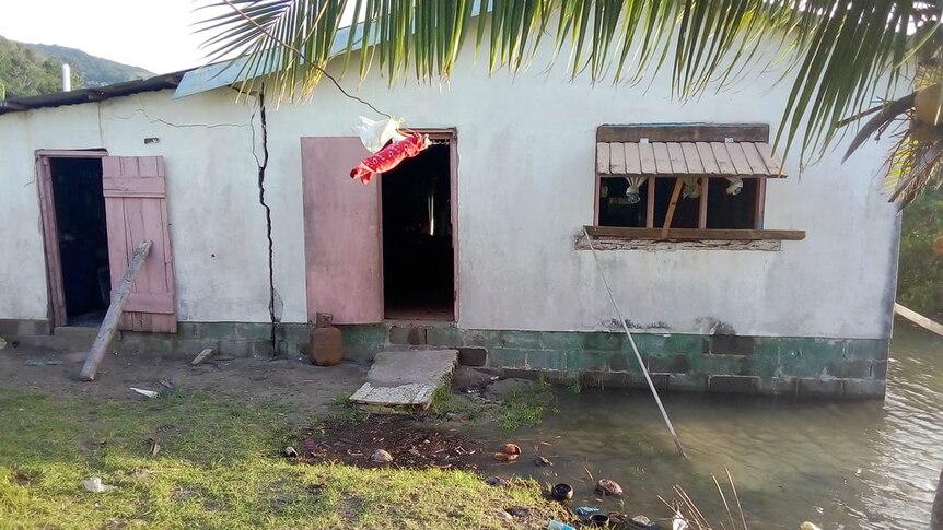 Clothes hang on a line in front of a small house with water lapping at the walls.