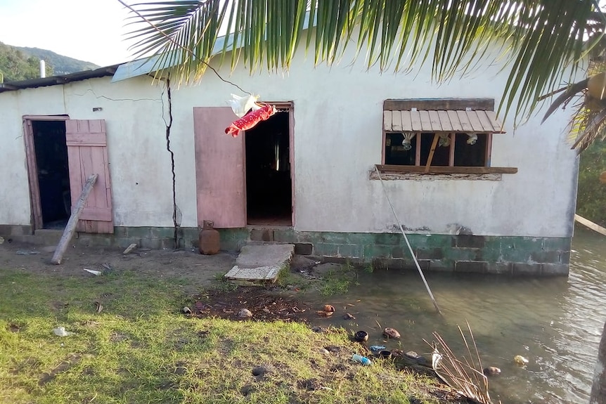 Clothes hang on a line in front of a small house with water lapping at the walls.