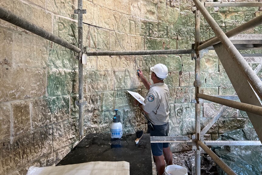A man standing inside a stone tower examining inscriptions on the wall