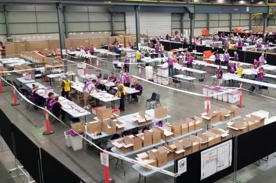 AEC staff count ballot papers in a large, industrial warehouse in Australia.