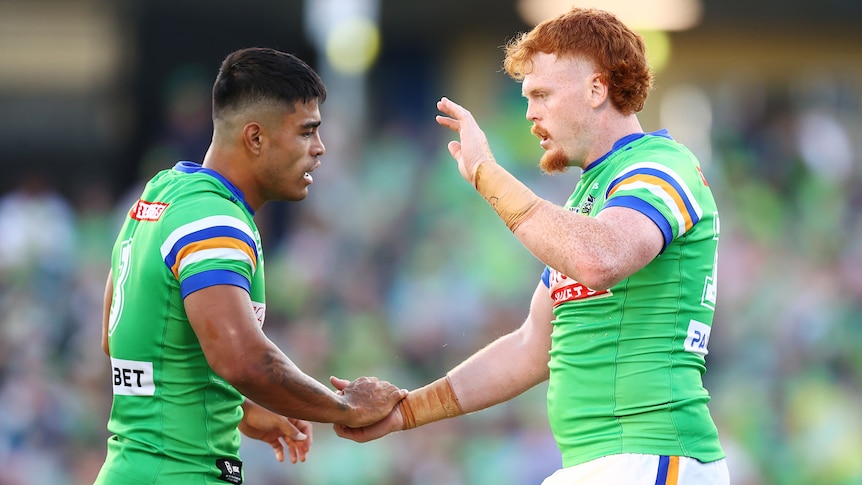 Two Canberra Raiders NRL players shake hands as they celebrate a try against Cronulla.