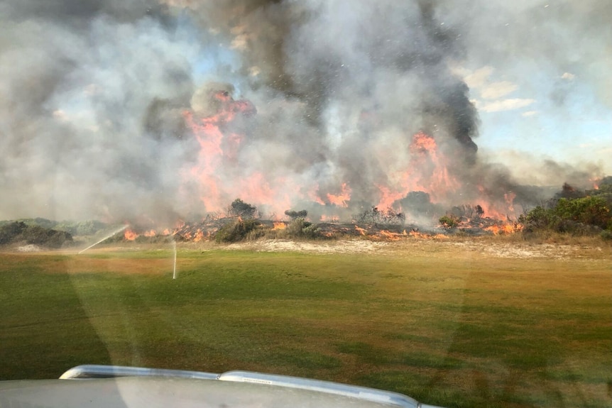 Red flames and smoke of a bushfire on the edge of a golf course.