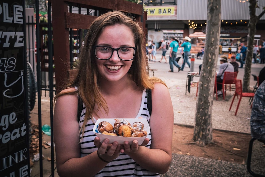Darcy Phillips smiles at the camera while holding a serving of deep fried Oreos
