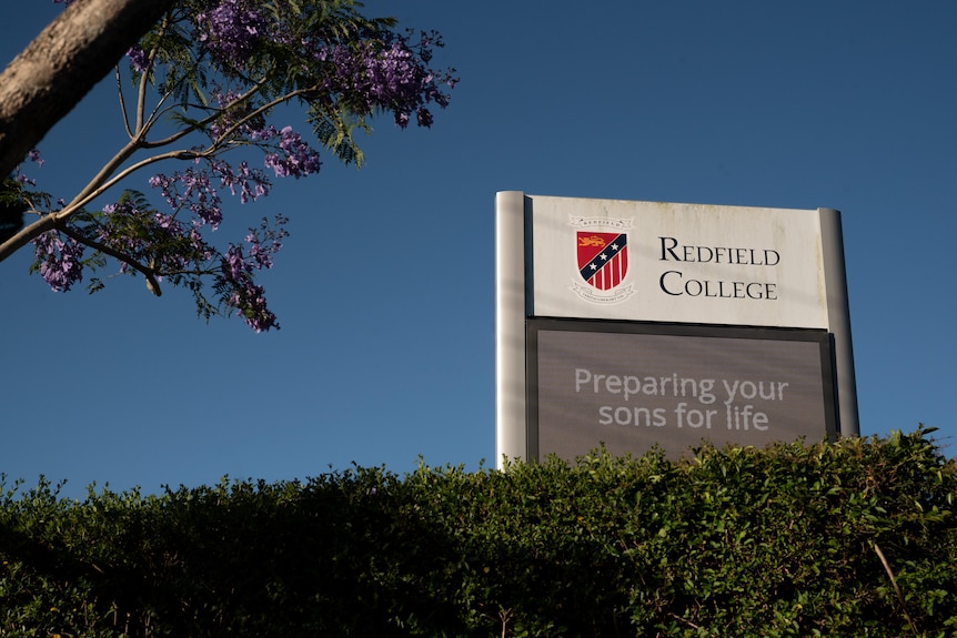 An electronic Redfield College school sign over a hedge with the words "Preparing your sons for life".