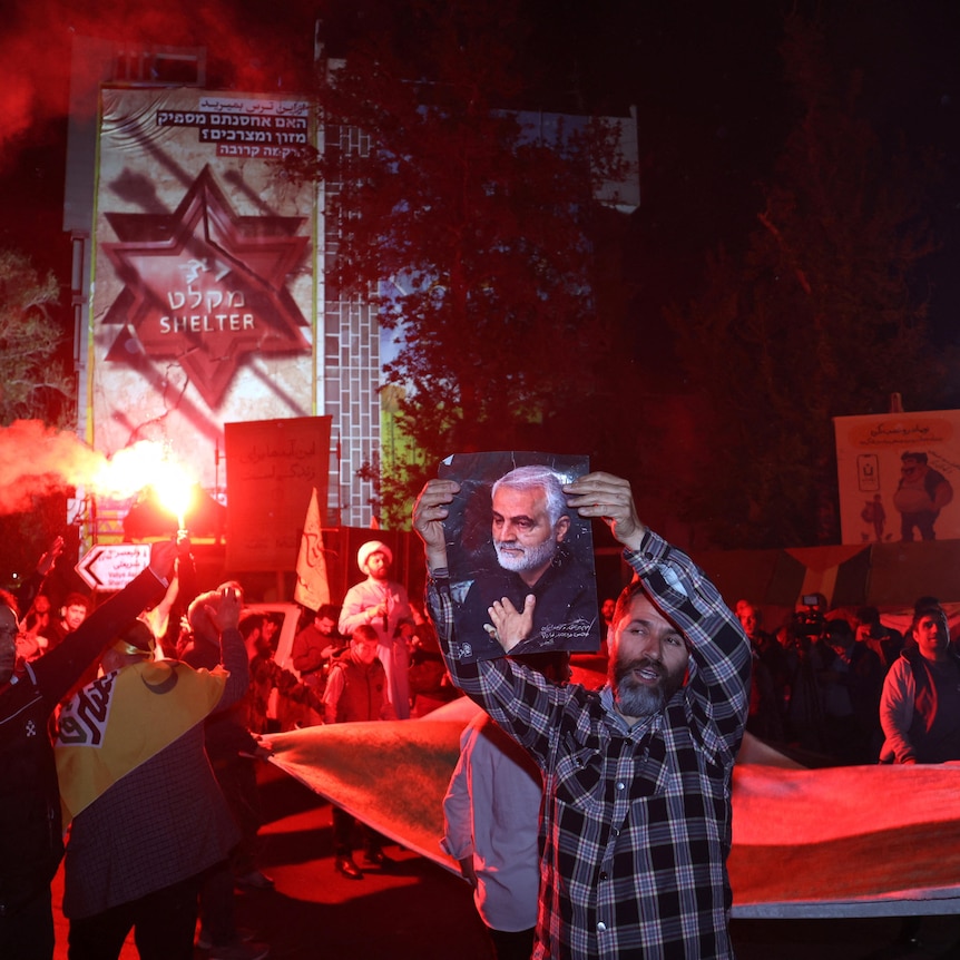 People standing outside with flares holding up pictures and posters.