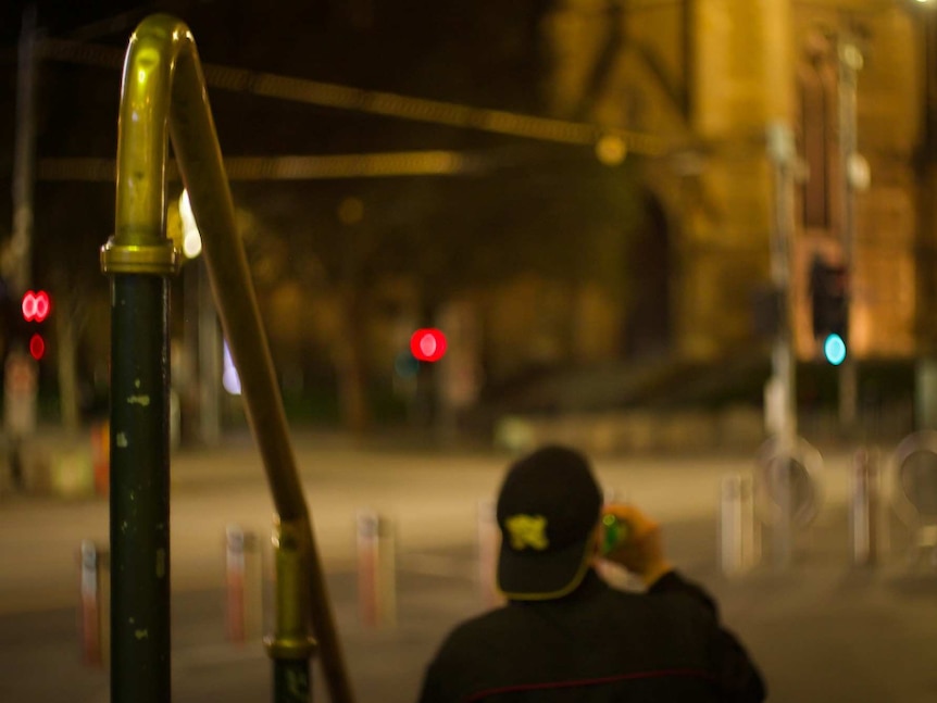 A person can be seen sitting on the steps of Flinders Street Station at night, with St Paul's Cathedral in the background.