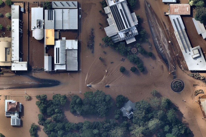 Several buildings including a city hall are seen from above, surrounded by floodwaters.