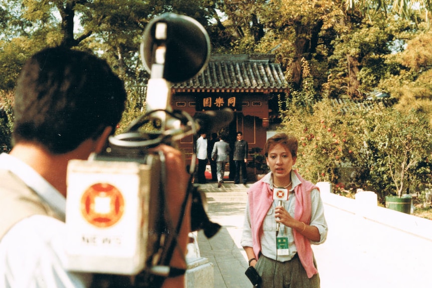 Young Hutcheon holding microphone and talking to camera in garden setting.