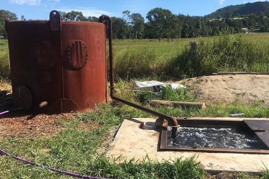 A rusted tank and an undergound tank connected by a large hose in a paddock.