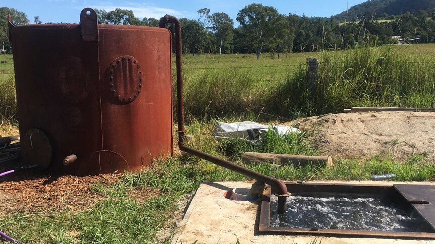 A rusted tank and an undergound tank connected by a large hose in a paddock.