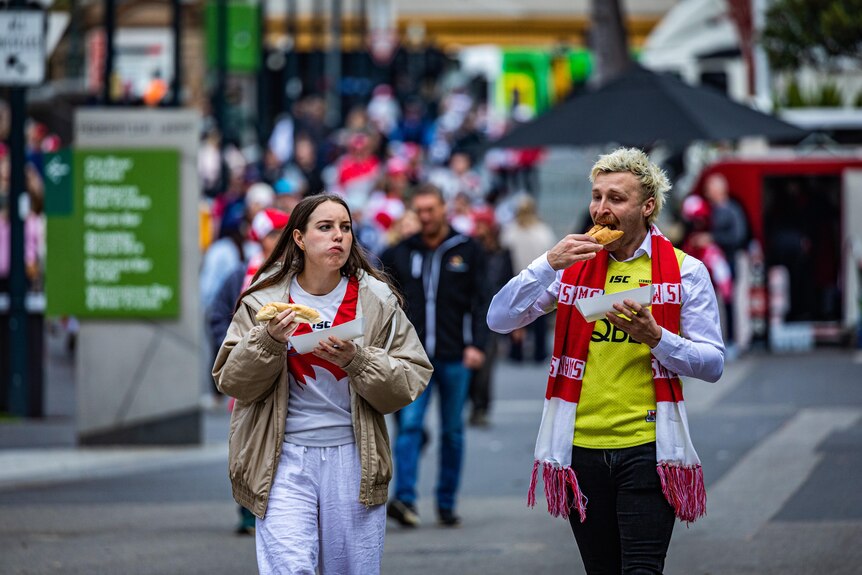 Two people eating and wearing Sydney Swans merchandise