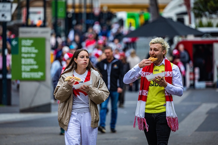 Two people eating and wearing Sydney Swans merchandise