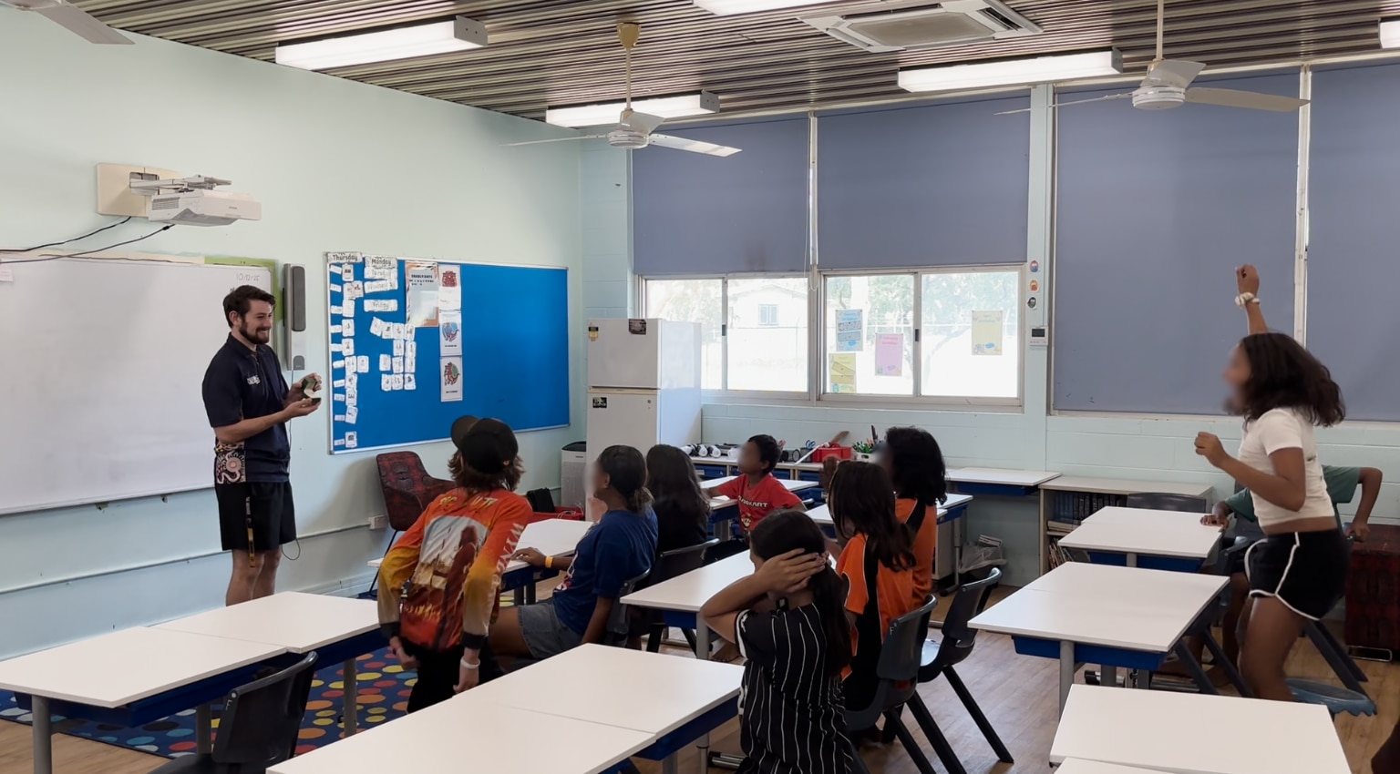 Un hombre y una mujer sonrientes levantando la mano con un anillo de compromiso frente a los estudiantes