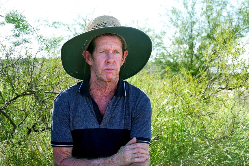 Paul Keegan in large hat kneels in front of some bushes