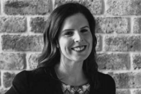 A black and white photo of a lawyer with long brown hair smiling at the camera in front of a brick wall