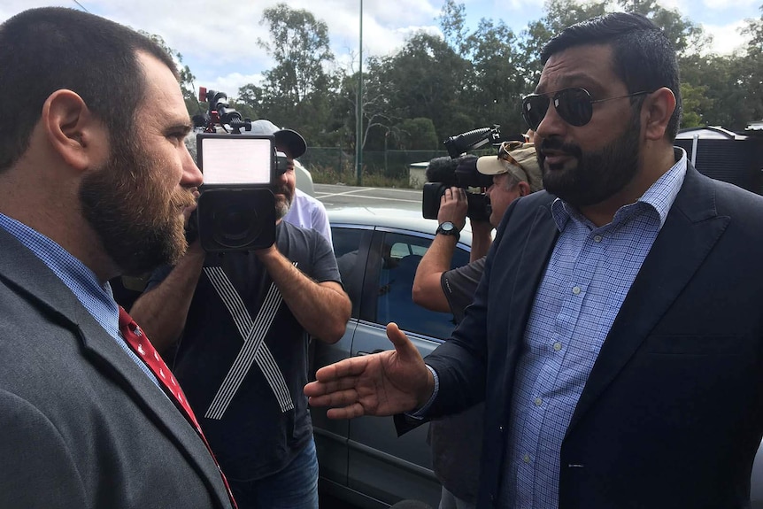 Two men speaking surrounded by media cameras