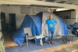 A man stands in front of the tent he has been forced to live in because of flooding.