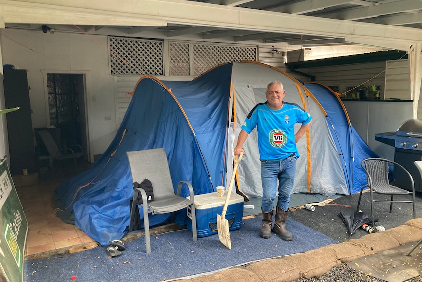Jamie Haycock standing infront of a tent he lives in, in his backyard, as he rebuilds is flood damaged home.