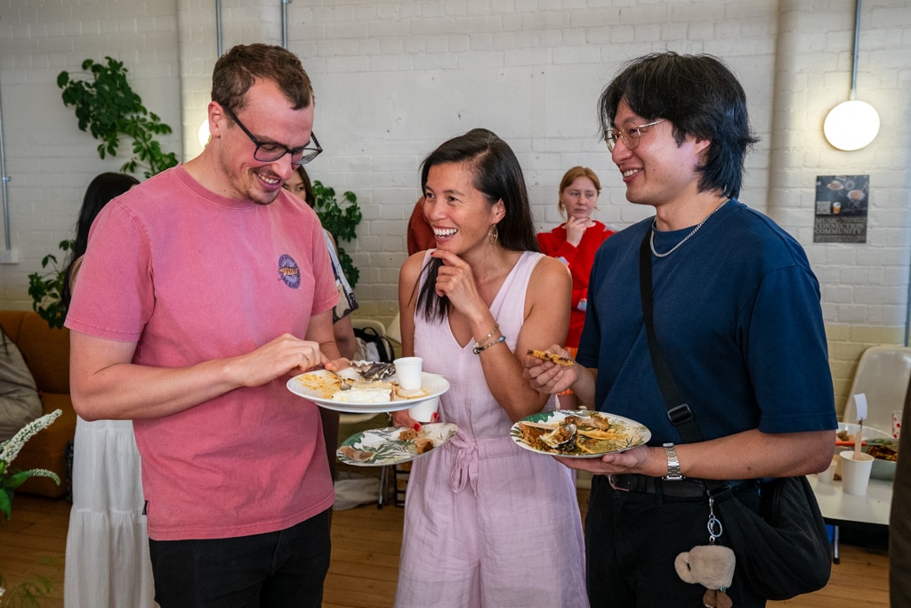Three people with plates of food stand chatting and laughing