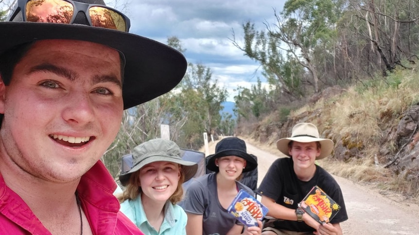 Daniel Forrest and three friends smile as they sit on camping chairs in the bush.