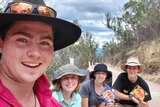 Daniel Forrest and three friends smile as they sit on camping chairs in the bush.