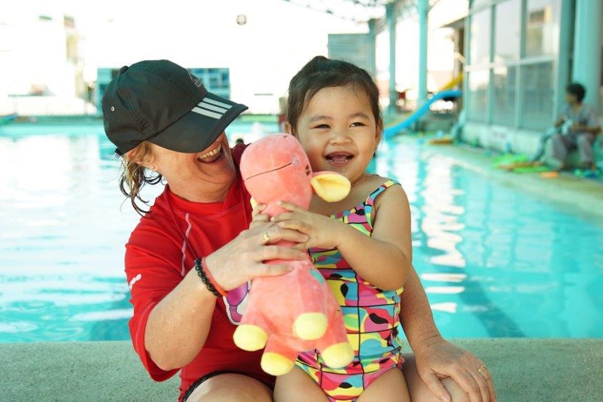 Swimming teacher with young student next to pool