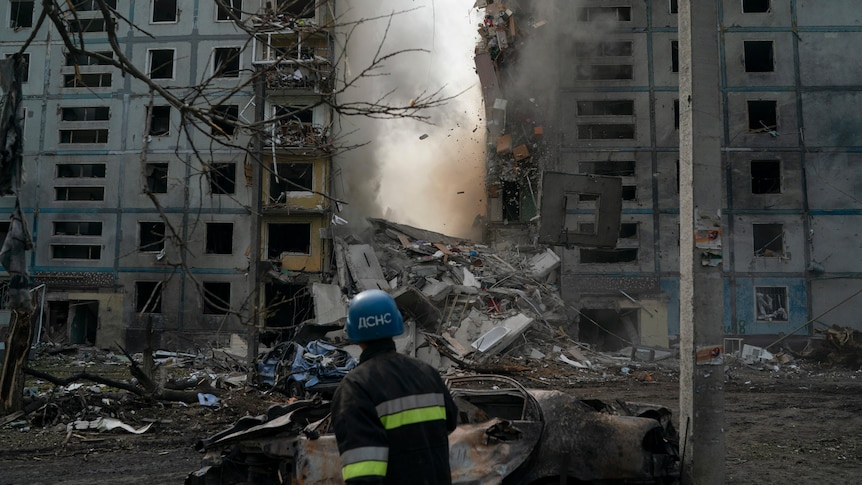 A firefighter looks at a part of a wall falling from a residential building