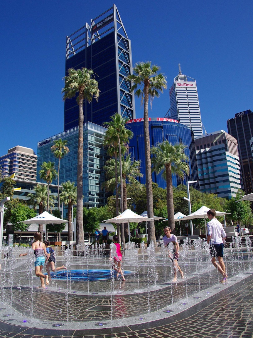 Children playing at the Elizabeth Quay water park in Perth with tall city buildings in the background.