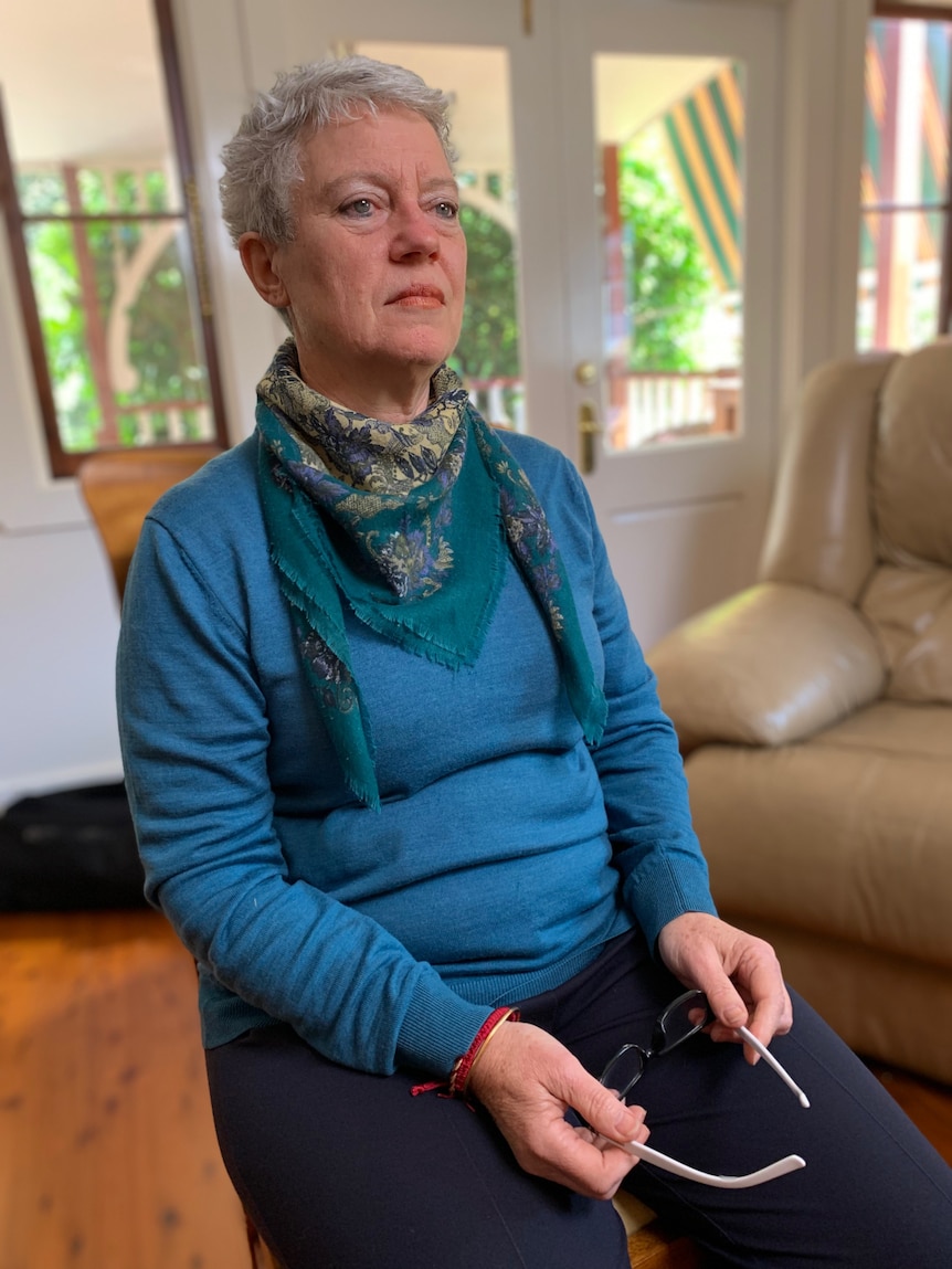 A woman sitting on a chair, holding her glasses.