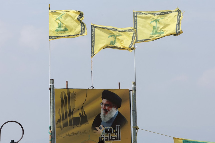 Three Hezbolah flags fluttering above a poster depicting Lebanon's Hezbollah leader Sayyed Hassan Nasrallah