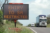 An electronic sign saying "entry to SA restricted" as a truck goes past in the opposite direction