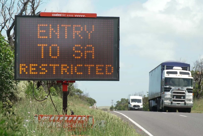 An electronic sign saying "entry to SA restricted" as a truck goes past in the opposite direction