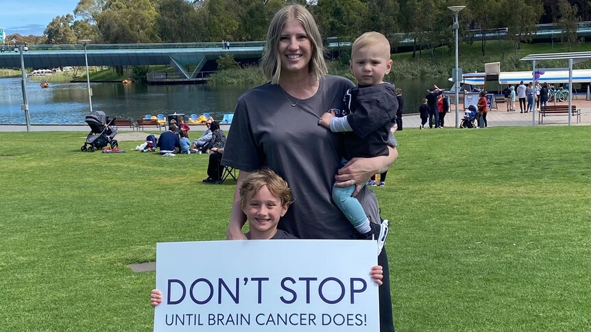 A woman with her two children holding a sign that reads don't stop until brain cancer does. 