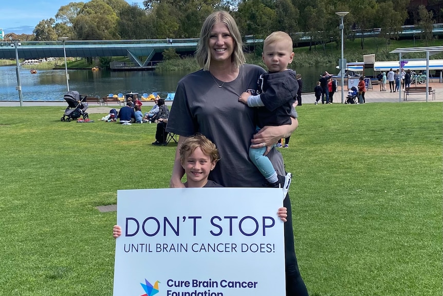 Kobieta z dwójką dzieci trzyma tabliczkę z napisem Nie przestawaj, dopóki rak mózgu nie ustanie. 