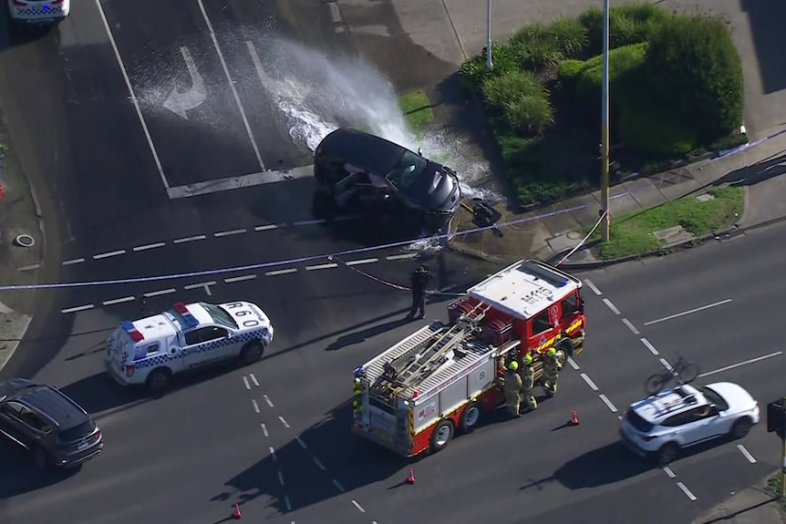 An aerial shot of a car crashed into a fire hydrant with emergency service cars nearby.