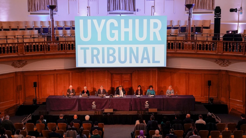 Seated panel of tribunal members with large sign behind with "Uyghur Tribunal' written.