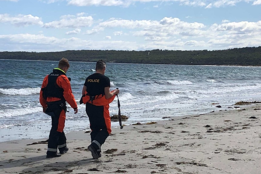 Two men wearing police-branded clothing walk along a beach