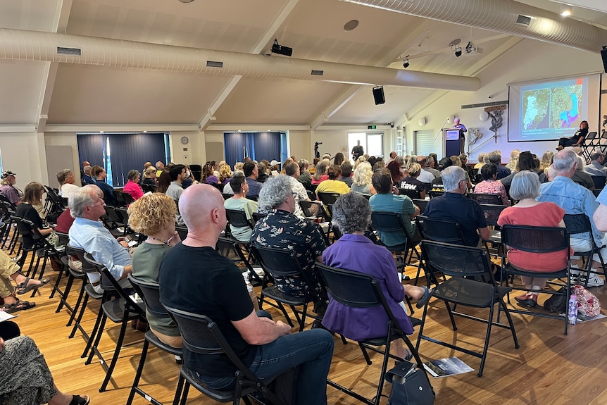 People sitting in rows watching speaker on stage.